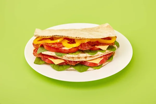 Fresh sandwich with salami, pita, vegetables and cheese on plate on green background — Stock Photo