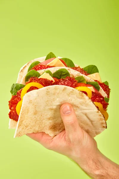 Частичный вид человека, держащего свежий сэндвич с салями, пита, овощи и сыр изолированы на зеленый — стоковое фото
