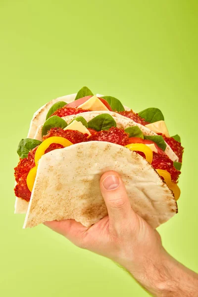Partial view of man holding fresh sandwich with salami, pita, vegetables and cheese isolated on green — Stock Photo