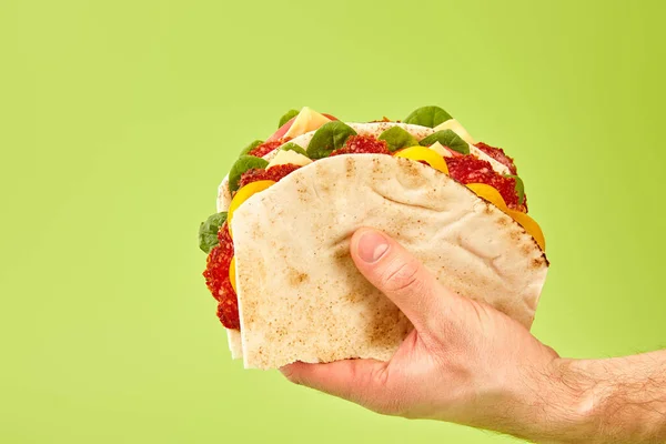 Partial view of man holding fresh sandwich with salami, pita, vegetables and cheese isolated on green — Stock Photo