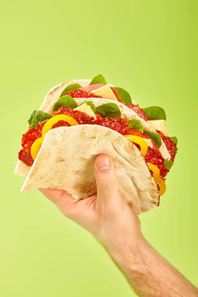 Частичный вид человека, держащего свежий сэндвич с салями, пита, овощи и сыр изолированы на зеленый — стоковое фото