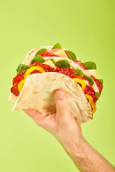 Partial view of man holding fresh sandwich with salami, pita, vegetables and cheese isolated on green — Stock Photo