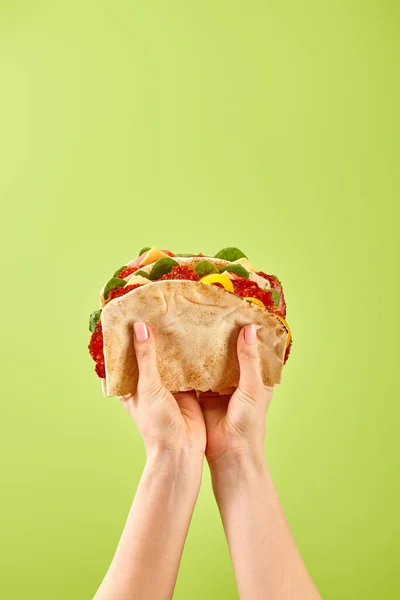 Partial view of woman holding fresh sandwich with salami, pita, vegetables and cheese isolated on green — Stock Photo