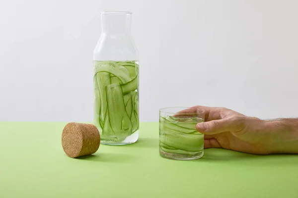 Vista recortada del vaso de mano masculino con bebida hecha de pepinos cortados en rodajas aislados en gris - foto de stock