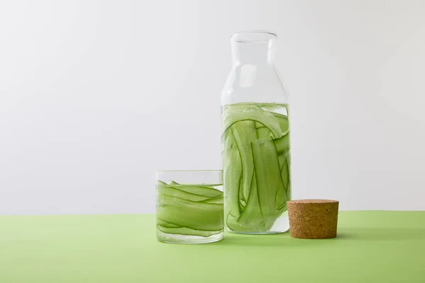 Bottle and glass with drink made of sliced cucumbers isolated on grey — Stock Photo