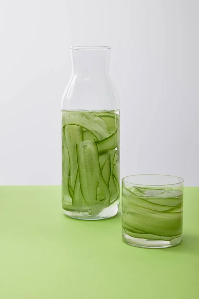 Bottle and glass with drink made of sliced cucumbers isolated on grey — Stock Photo