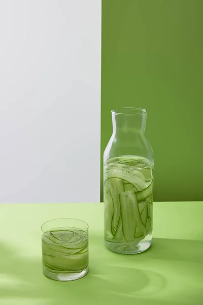 Высокий угол обзора бутылки и стекла с напитком из нарезанных огурцов на сером и зеленом фоне — стоковое фото
