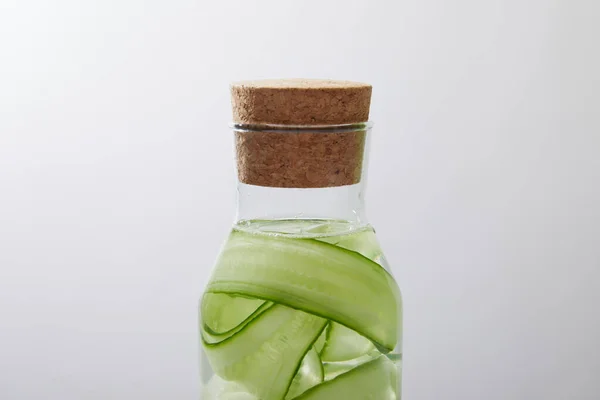 Vista da vicino bottiglia di vetro con tappo di sughero con bevanda a base di cetrioli tagliati isolati su grigio — Foto stock