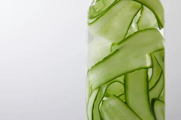 Close up view of glass bottle filled with liquid and sliced cucumbers isolated on grey — Stock Photo