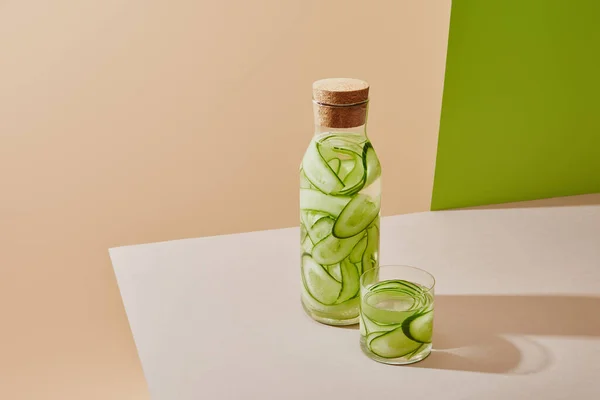 High angle view of glass and bottle with cork filled with fresh water and sliced cucumbers on table on beige and green background — Stock Photo