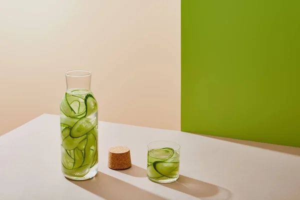 High angle view of cork, glass and bottle filled with water and sliced cucumbers on table on beige and green background — Stock Photo