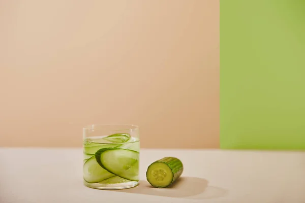 Glass of detox drink and sliced cucumbers on beige and green background — Stock Photo