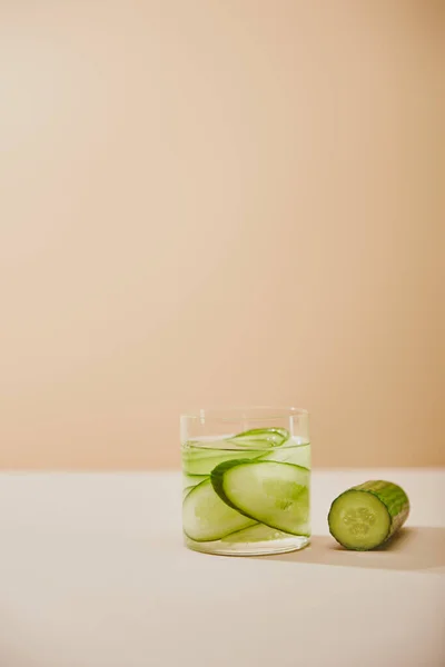 Glass of water with sliced cucumbers on table isolated on beige — Stock Photo