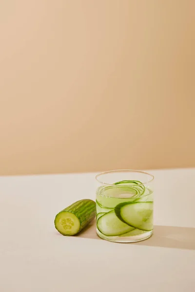 Hochwinkel-Ansicht des Wasserglases mit Gurkenscheiben auf dem Tisch isoliert auf beige — Stockfoto