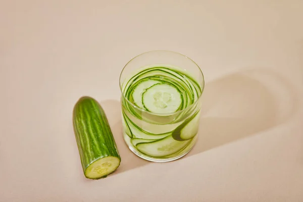 High angle view of glass with detox drink and sliced cucumbers on table on beige background — Stock Photo