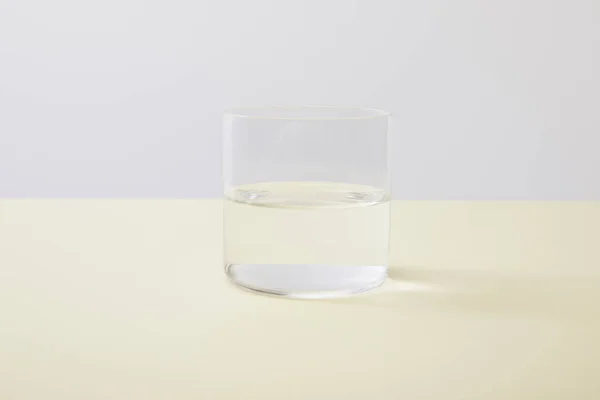 Vidrio con agua sobre superficie amarilla aislada sobre gris - foto de stock