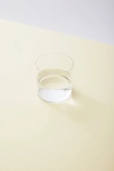 Vue grand angle du verre avec de l'eau sur la surface jaune isolé sur gris — Photo de stock