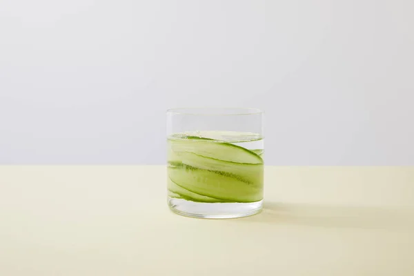 Glass with fresh water and sliced cucumbers on yellow surface isolated on grey — Stock Photo