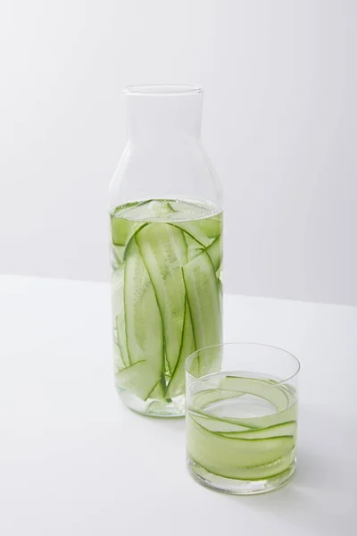 Vista de alto ángulo de botella y vidrio con agua y pepinos en rodajas aislados en gris - foto de stock