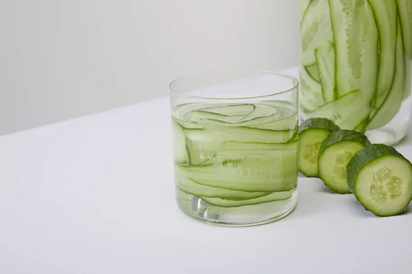 Vista de cerca de la botella recortada y el vidrio con bebida fresca de desintoxicación y pepinos en rodajas aislados en gris - foto de stock