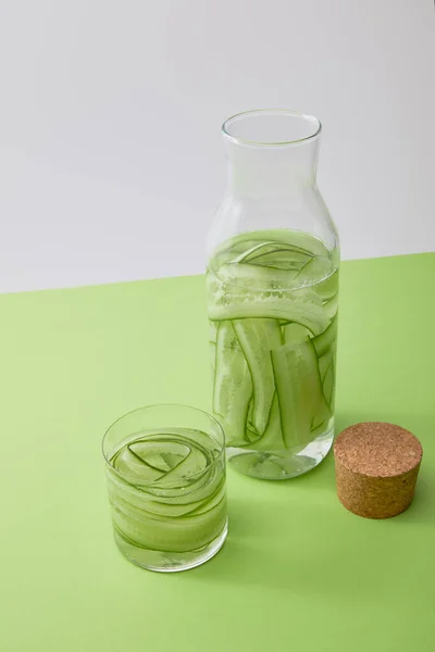 Vue grand angle du liège, du verre et de la bouteille avec de l'eau et des concombres tranchés isolés sur gris — Photo de stock