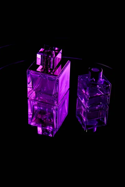 Frascos de perfume roxo na superfície escura espelho isolado em preto — Fotografia de Stock