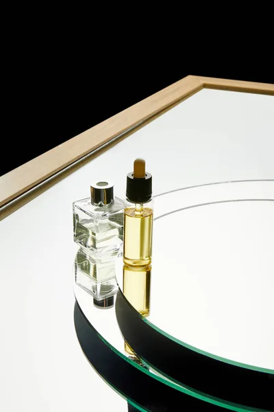 Високий кут зору на ароматну пляшку парфумів і пляшку сироватки на дзеркальній поверхні ізольовані на чорному — стокове фото