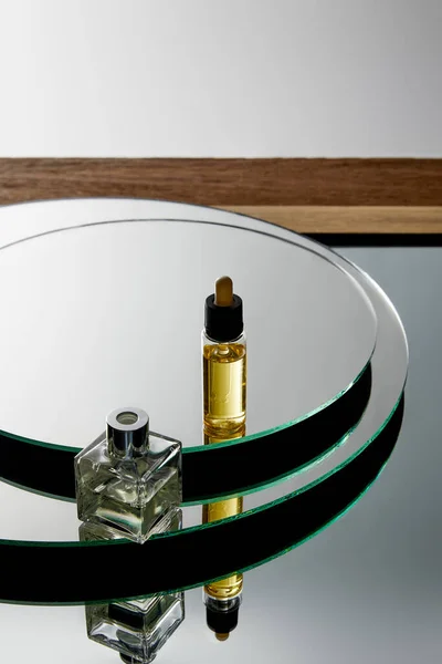 Vista de ángulo alto de la botella de perfume y botella de suero con aceite en la superficie del espejo - foto de stock