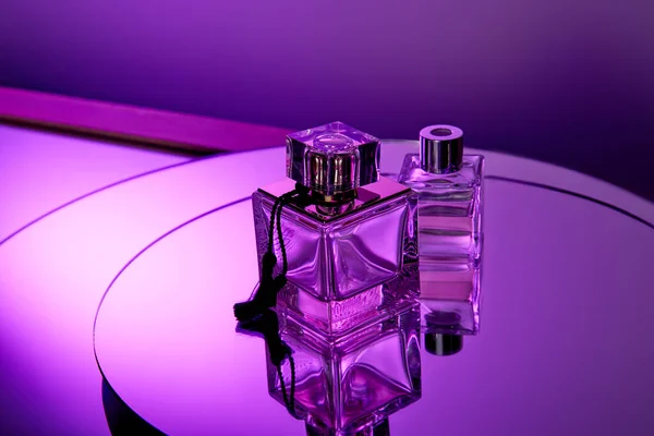 Фиолетовые стеклянные духи бутылки на круглой фиолетовой поверхности зеркала с отражением — стоковое фото