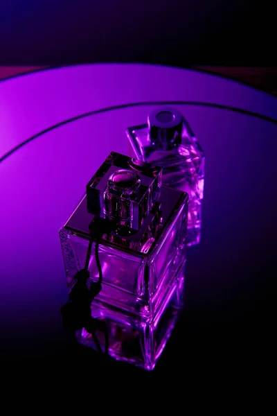 Vista dall'alto di bottiglie di profumo sulla superficie dello specchio rotondo viola scuro drammatico — Foto stock