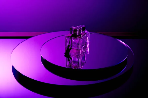 Violet luxury perfume bottles on round mirror surface with reflection isolated on purple — Stock Photo