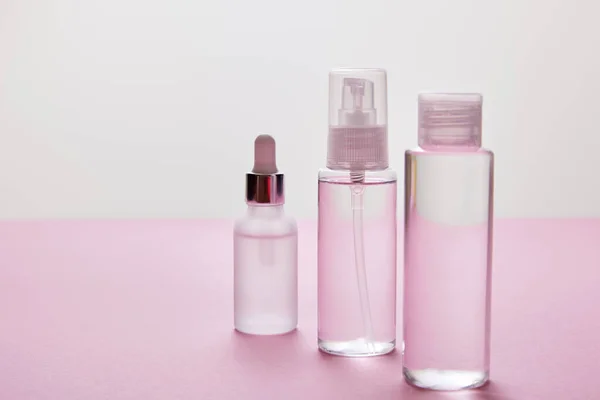 Spray, botella cosmética y botella de suero con líquido sobre fondo rosa y gris - foto de stock