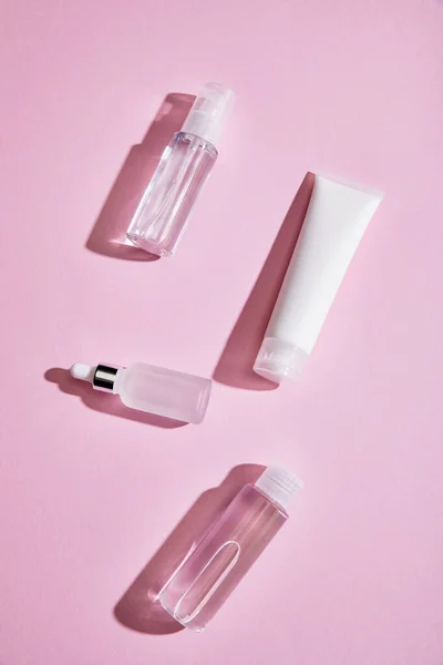 Top view of cream tube, cosmetic bottle, spray and serum bottles with liquid on pink background — Stock Photo