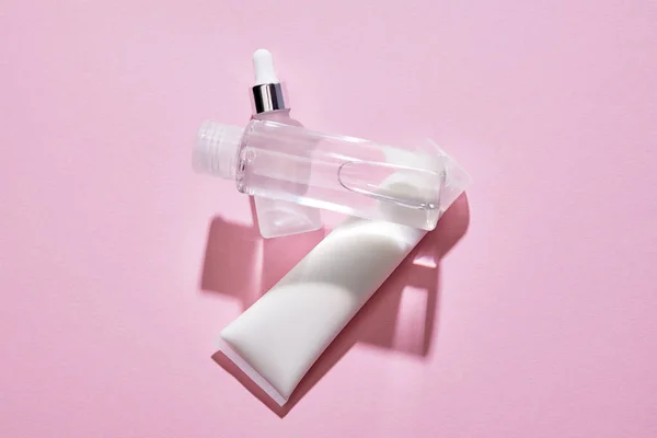 Visão superior do tubo de creme de mão, garrafa de cosméticos e frasco de soro com líquido no fundo rosa — Fotografia de Stock