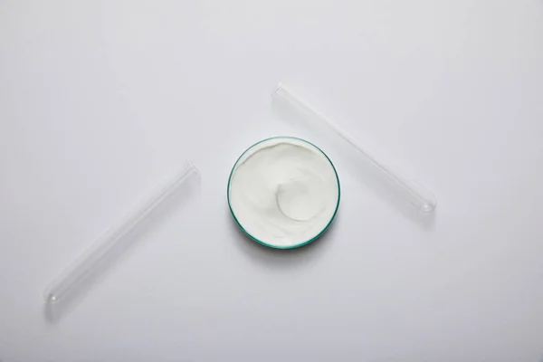 Vue du dessus de la verrerie de laboratoire avec crème cosmétique blanche et éprouvettes sur fond gris — Photo de stock