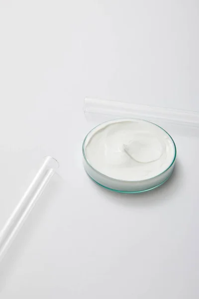 Artículos de vidrio de laboratorio con crema cosmética blanca y tubos de ensayo sobre fondo gris - foto de stock