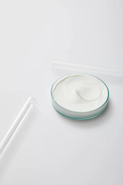 Vidros de laboratório com creme cosmético branco e tubos de ensaio sobre fundo cinzento — Fotografia de Stock