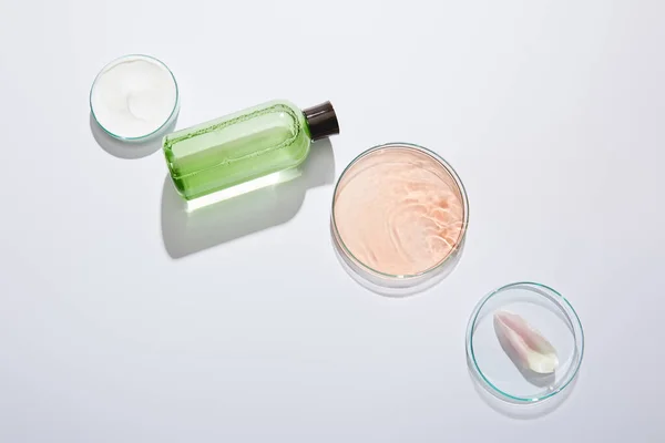 Flache Lage mit Laborgläsern, Kosmetikflasche mit grüner Flüssigkeit, Kosmetikcremedose und Rosenblütenblatt auf grauem Hintergrund — Stockfoto