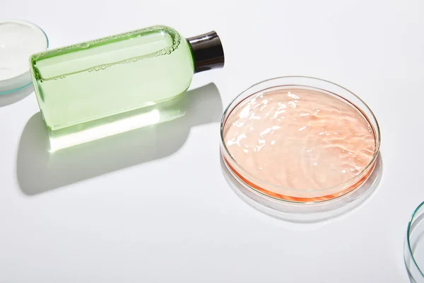 Kosmetikflasche mit grüner Flüssigkeit und Laborgläser mit flüssiger und kosmetischer Creme auf grauem Hintergrund — Stockfoto