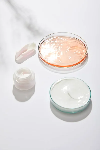Laborgläser mit kosmetischer Creme und Flüssigkeit und Rosenblatt auf weißem Hintergrund mit Schatten — Stockfoto