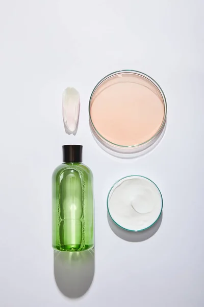 Posa piatta con bottiglia cosmetica con liquido verde, vaso con crema cosmetica bianca e vetreria da laboratorio con liquido su fondo grigio — Foto stock