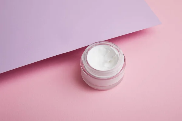 Kosmetische Creme im Glas auf rosa und lila Hintergrund — Stockfoto