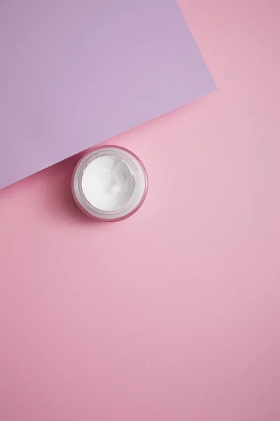 Top view of cosmetic cream in glass jar on pink and lilac background — Stock Photo