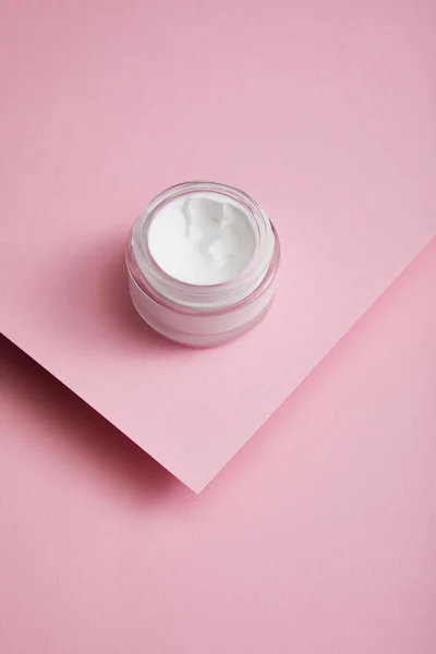 Высокоугловой вид косметического крема в стеклянной банке на структурированном фоне из розовой бумаги — стоковое фото