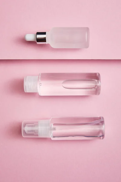 Asiento plano con botella cosmética, spray y suero sobre fondo rosa y gris - foto de stock