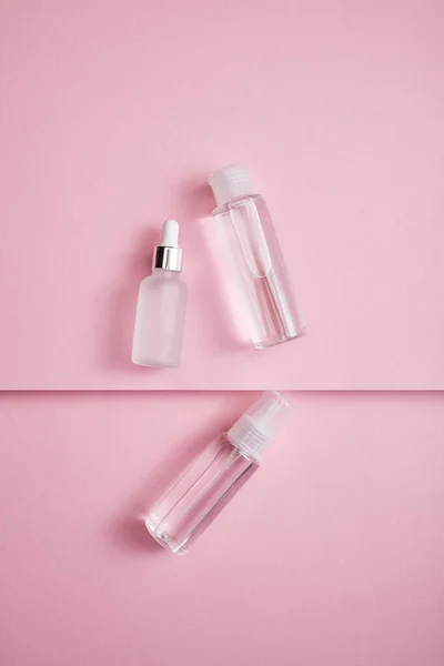 Vue du dessus du flacon cosmétique transparent, du vaporisateur et du flacon de sérum avec liquide sur fond de papier rose — Photo de stock