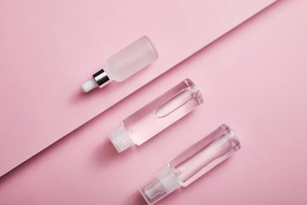 Flat lay with cosmetic bottle, spray and serum bottle with liquid on pink background — Stock Photo