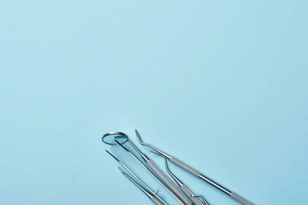 Високий кут огляду металевих професійних стоматологічних інструментів на синьому фоні — стокове фото