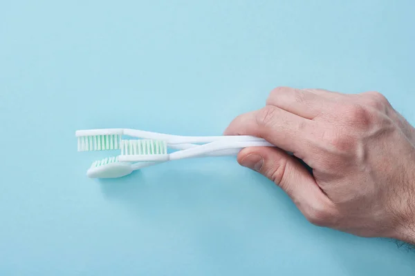 Cropped view of man holding white toothbrushes on blue background — Stock Photo