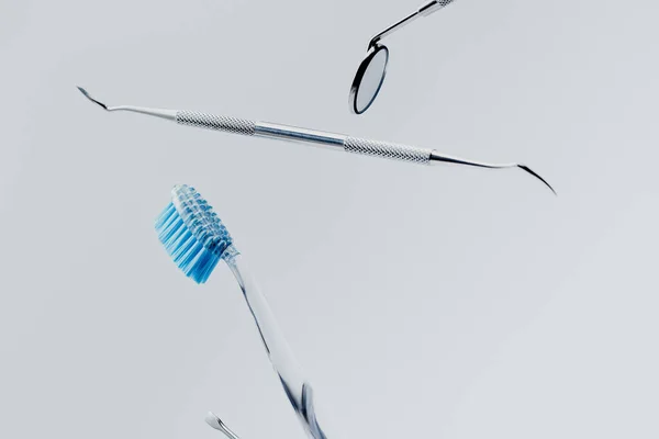 Стоматологические инструменты и зубная щетка с голубой щетиной левитации изолированы на сером фоне — стоковое фото